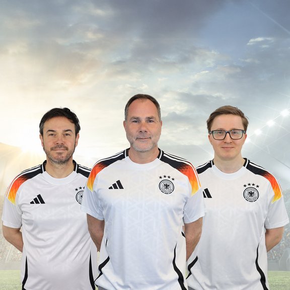 The picture shows Iljan Sandtstedt, Thomas Kolossa and Nicolas Wiacker in Germany football shirts. They have their arms crossed behind their backs and are smiling friendly into the camera.