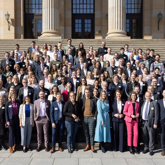 Auf dem Bild ist eine große Gruppe von Menschen auf einer Treppe vor den Säulen eines großen Gebäudes zu sehen.