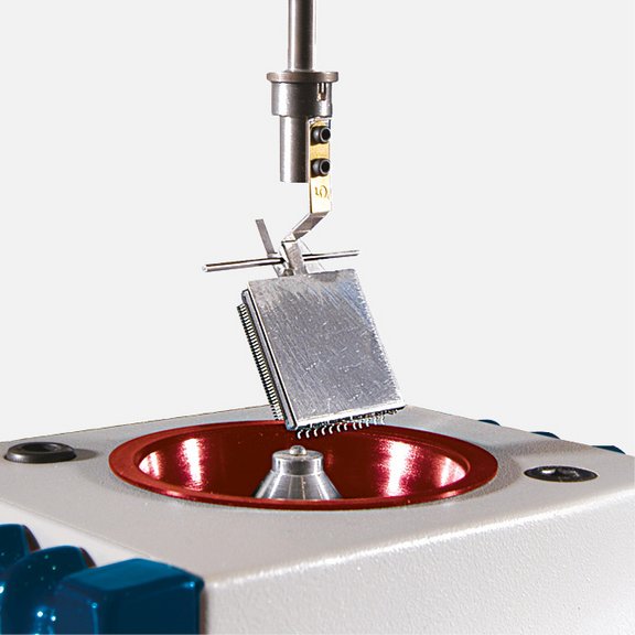 The picture shows a wetting scale: A component is attached to a holder and is slowly lowered onto a small solder ball.
