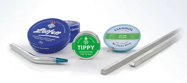 The picture shows various accessories, such as a round, blue tin of soldering grease, a small, round metal tin of Tippy soldering tip cleaner, a replacement soldering tip and a roll of desoldering wick.
