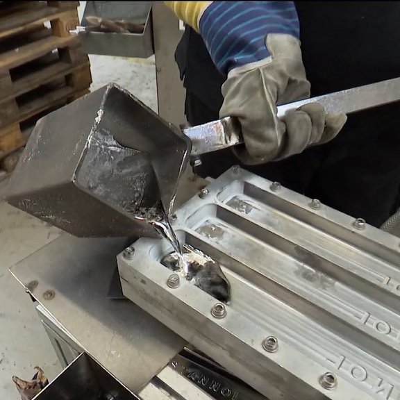 The picture shows a mould into which liquid tin is being poured.