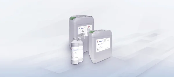 The image shows three large canisters and two bottles of Flux-Ex cleaning agents from the Stannol brand. The canisters are gray with green caps, and the labels display product names such as "Flux-Ex Post Power" and "Flux-Ex Glue." In front of the canisters are two white bottles, one with a spray nozzle, also featuring the Stannol logo and descriptions. These products are professional cleaning agents used in the soldering industry.