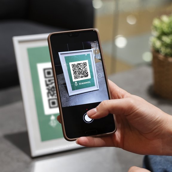 The picture shows a hand holding a smartphone that is scanning a QR code.