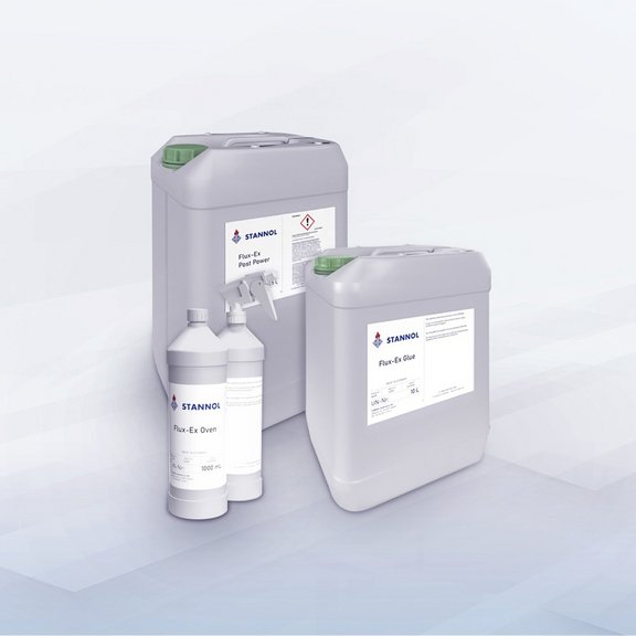 The picture shows three large canisters and two bottles of Flux-Ex cleaning agent from the Stannol brand. The canisters are grey and have green caps, with product names such as ‘Flux-Ex Post Power’ and ‘Flux-Ex Glue’ on the labels. In front of the canisters are two white bottles, one of which has a spray nozzle, also with the Stannol logo and labelling. The products are professional cleaning agents for the soldering industry.