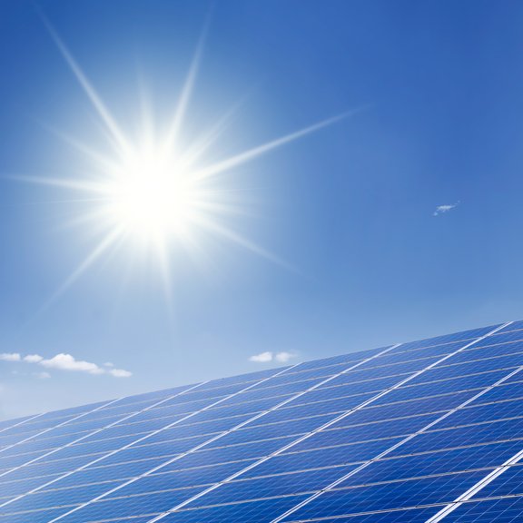The picture shows a PV system, a blue sky and a bright sun.