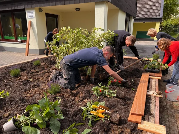 Auf dem Bild sind fünf Personen zu sehen, die ein Pflanzenbeet anlegen.